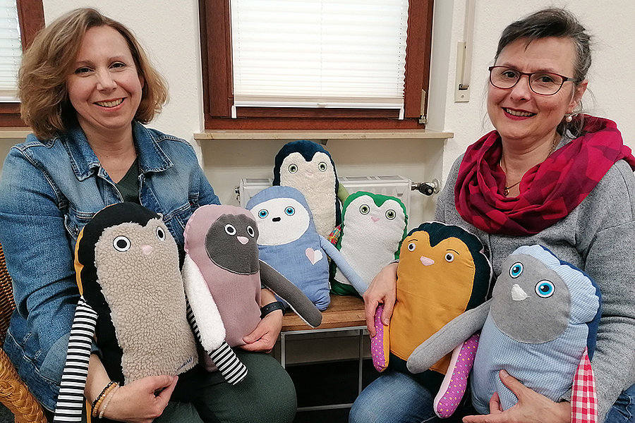 Zwei Frauen sitzen nebeneinander und halten bunte, handgemachte Plüschtiere in Form von Vögeln mit verschiedenen Farben und Mustern