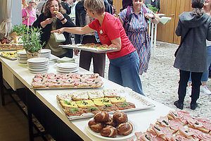 Buffet mit verschiedenen belegten Broten und Pilzen auf einem langen Tisch in einem Raum mit mehreren Personen im Hintergrund