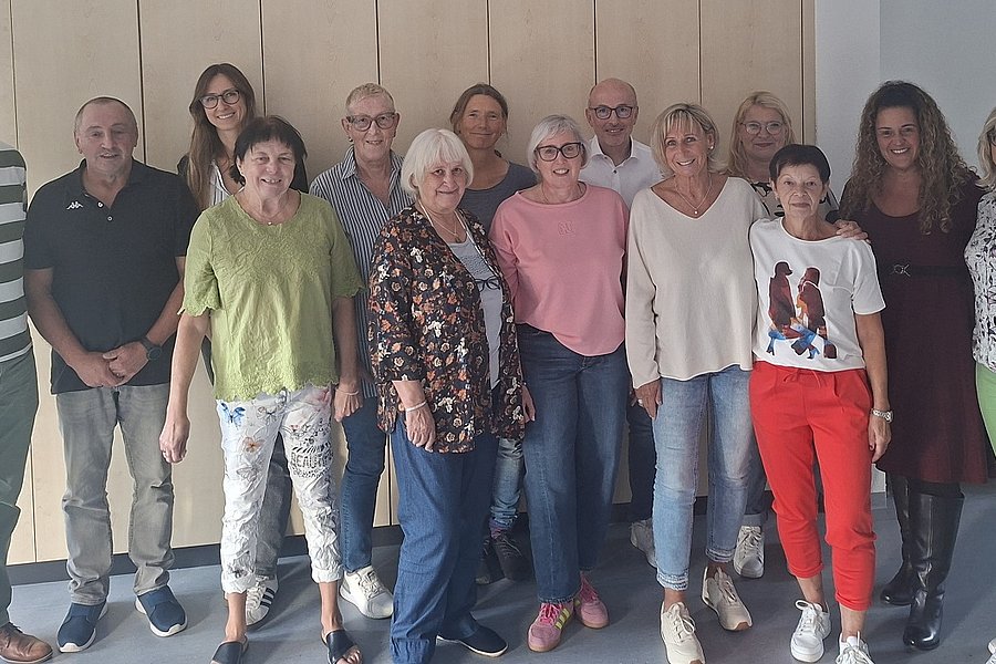 Gruppe von zwölf Personen steht nebeneinander vor einer weißen Wand