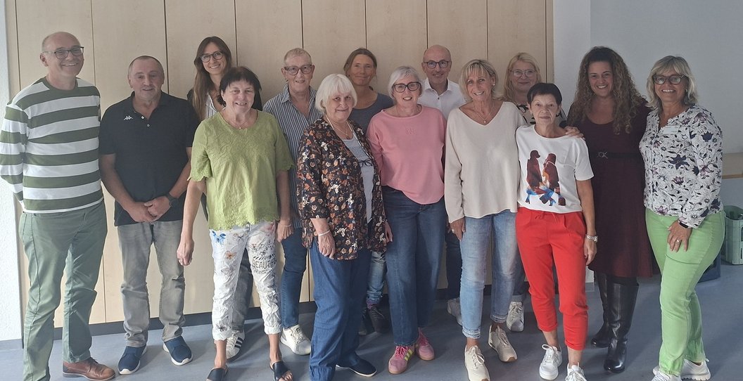 Gruppe von zwölf Personen steht nebeneinander vor einer weißen Wand