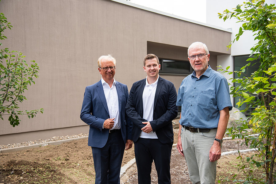 Drei Männer in Business- und Freizeitkleidung stehen vor einem modernen Gebäude im Freien