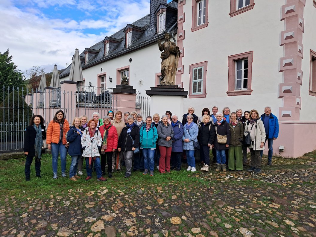 Gruppe von Menschen vor einem historischen Gebäude mit rosa-weißen Fassadenelementen und einer Statue auf einem Sockel im Hintergrund.