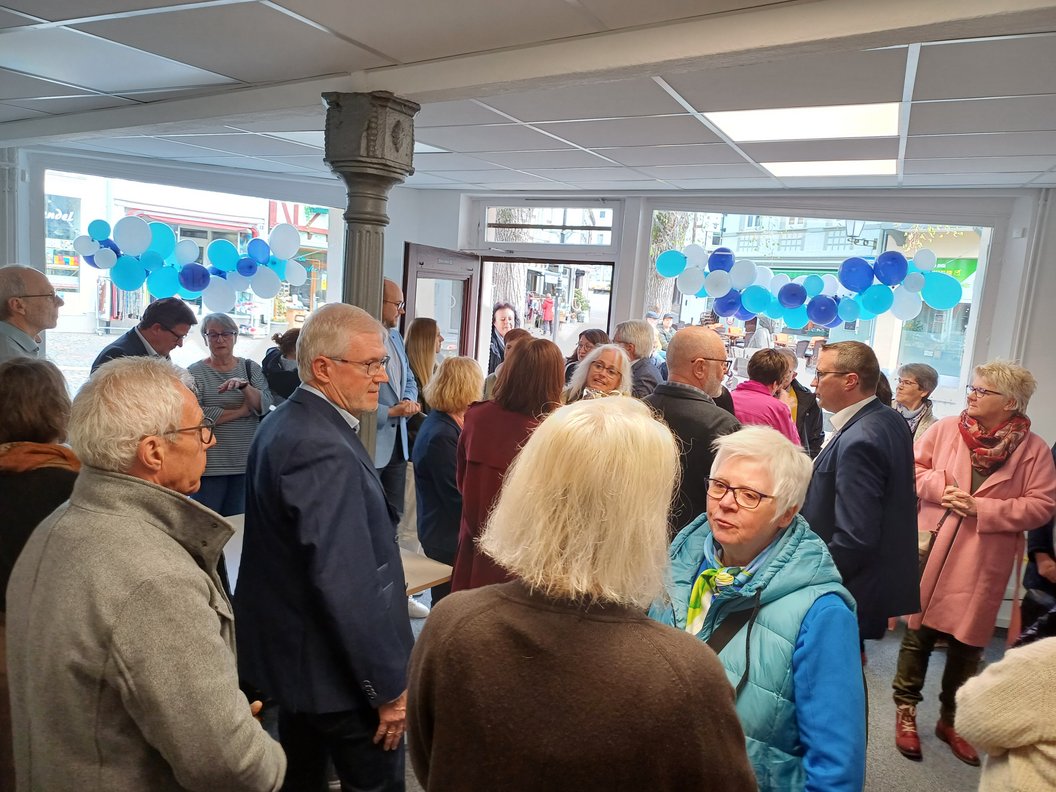 Menschen in einem Raum mit blauen Luftballons an den Fenstern, die sich unterhalten und austauschen