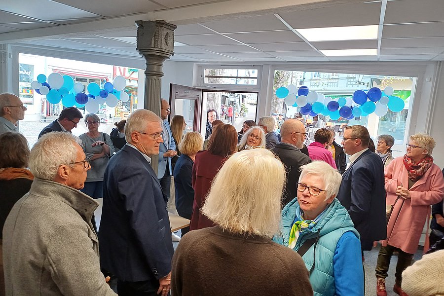 Menschen in einem Raum mit blauen Luftballons an den Fenstern, die sich unterhalten und austauschen