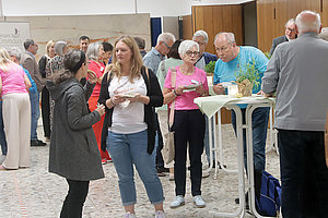 Soziale Veranstaltung mit Gästen, die Snacks essen und miteinander sprechen, in einem hellen Raum.