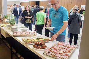 Mehrere Personen bedienen sich an einem langen Buffet mit belegten Broten und Brötchen in einem Saal mit Holzvertäfelung